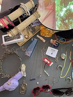 Photo of assorted bracelets on display stands, various necklaces laid out, red heart-shaped sunglasses, rings, pendants, and other costume jewelry pieces.
