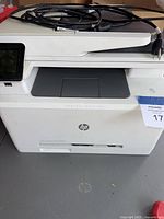Front view of white HP Color LaserJet Pro MFP M277dw with touchscreen panel and power cord placed on top