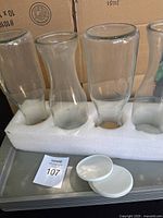 Four glass juice carafes held in white foam, stacked behind cardboard boxes.