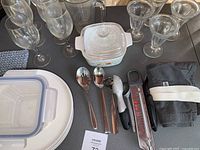 Photo depicting glassware, storage containers, CorningWare lidded dish, and kitchen utensils arranged on table.