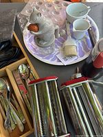 Photo showing the Imperial pasta maker alongside other kitchen items including silverware, plastic molds, and a patterned tray