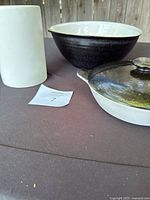 Photo of the white matte crock, black bowl with white interior, and black and white covered round dish with knob lid arranging on a brown surface.