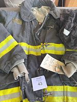 Front view of NYFD turnout coat showing yellow reflective stripes, heavy wear, and attached paper note with size.