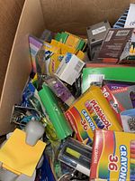 Box filled with various office supplies including crayons, pencils, stationery items, highlighters, and clips.