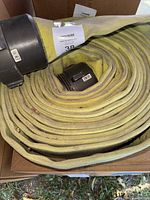 Coiled yellow fabric fire hose with large metal coupling in foreground.