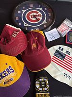 Photo showing 4 sports hats, Boston Bruins sock, USA swimming cap, Chicago Cubs clock.