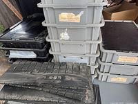 Stacked gray and black plastic storage bins with some flat covers and lids visible, dust on lids and bins.