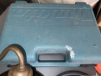 Blue plastic case with Makita brand debossed on top and portion of a brass object visible