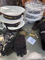 Photo showing stacked white sailor hats with Green Zephyr Lines black bands, name badges, gloves and part of tactical shirts with labels visible.