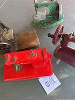 Top-down view of four vintage children's toy sewing machines in a box, including red, green, maroon, and smaller plain metal machines.