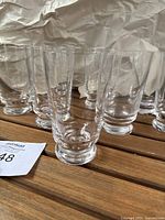Eight clear pedestal glasses displayed on wooden surface, showing sturdy bases and straight walls.