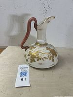 Front side of Harrach Bohemian art glass ewer showing gold floral motif and rust-colored handle.