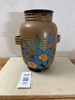 Front and side views of 13 inch tall pottery vase with brown matte glaze and colorful hand-painted blue and yellow flowers with green leaves. Vase has two small handles and flared mouth with ridges near top.