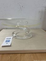Side view of transparent Lucite cake stand showing sculptural swirl base and round top