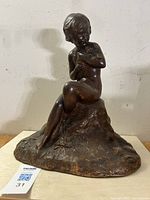 Front and side view of the dark brown terracotta sculpture showing a seated nude child holding flowers.