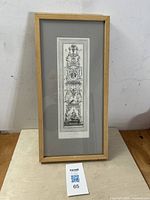 Framed vertical rectangular etching mounted on gray mat inside a light wooden frame, with the artwork showing classical arabesque and ornamental designs and a medallion portrait.