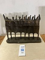 Front view of the bronze patina Brutalist sculpture with multiple elongated abstract figures on a flat base.