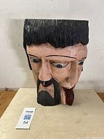 Front and side views of the painted dual-faced wood sculpture showing carved details, hair texture, and facial expressions.