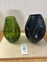 Pair of sculptural mid-century art glass vases, one green Blenko and one dark smoke jade Empoli, shown side by side on light surface against a white wall.
