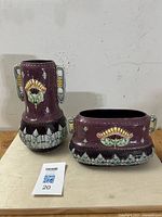 Full view of the pair, showing vase and planter with floral motifs and handles on a beige surface against a white wall.