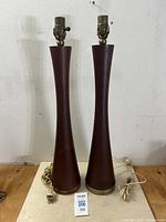 Full view of the pair of teak table lamps on a wooden surface showing their tapered flared bodies and brass socket tops with attached cords.