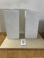 Front view of pair of white porcelain vases with textured pattern standing side by side.