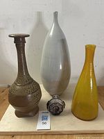 Four items on a wooden surface: tall brown textured pottery decanter, large white elongated vase, amber crackle glass decanter, small round snuff bottle with black Yin Yang design.