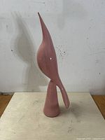 Full frontal photo of pink glazed mid-century modern ceramic bird sculpture with long neck and abstract tail on round base. Visible repair to beak tip.