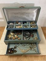Opened vintage blue jewelry box showing top tier with compartments filled with costume and sterling silver jewelry items.