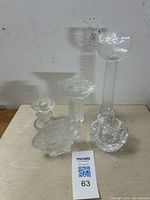 Five clear textured art glass pieces on a beige surface against a plain wall, including candlesticks, candleholders, and a fish figurine.