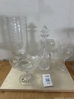 Full lot view showing five crystal and glass items on a wooden surface against a white wall.