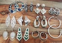 Photo showing 11 pairs of large chunky costume earrings in various designs and colors arranged on wooden surface.