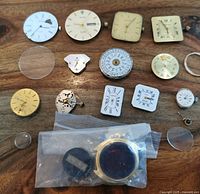 Top down photo of 13 quartz watch movements and components including dials, crystals, and cases