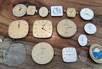 Top view of 14 quartz watch movements and dials arranged on a wooden surface showing various brands and styles.