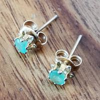 Close-up angled view of two 14k yellow gold emerald stud earrings on wooden surface, showing prong settings and butterfly backs.