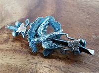 Front-side angled view of antique sterling silver brooch showing swallow bird, scalloped horseshoe, and gold leaves on wooden surface.