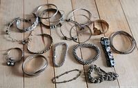 Overview of 19 silver-tone and gold-tone costume bracelets in various designs laid on wooden table