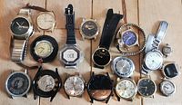 Top view showing all 19 watches arranged on wooden surface, various styles and conditions, some without bands