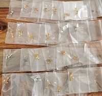 Top down view of 25 pairs of costume stud earrings individually bagged, showing mostly gold and silver-tone metal studs in various designs.