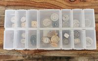 Top view of plastic storage box with 15 compartments holding vintage watch dials and movements in varied condition and styles.