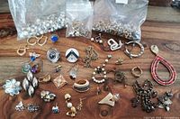 Multiple single earrings spread on wood surface with plastic bags of additional single earrings in the background.