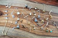 Overview of 29 assorted tie tacks, collar pins and stick pins laid out on a wooden surface showing the various styles and colors.