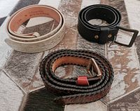Overview of the three coiled belts showing different colors and buckle types placed on a leather-patterned surface.