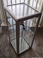Full view of the glass display case showing four glass shelves inside a metal frame with a locking front door.