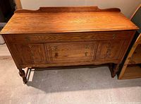 Front view of solid oak antique sideboard showing the carved detailing on doors and drawer fronts, and ornate handles.