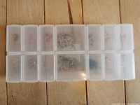 Top-down view of two rows of clear plastic compartment boxes filled with assorted watch hands.