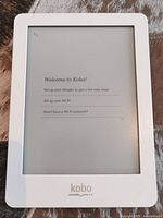 Front view of Kobo e-reader displaying setup screen with Kobo logo and Wi-Fi setup instructions, showing white bezel and e-ink display.