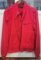 Red Member's Only windbreaker jacket displayed on hanger showing front with zipper and snap button closure, epaulets, and logo patch.