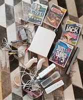 Lot arranged on carpet showing Nintendo Wii console, 4 game cases, 2 Wii Remotes, 2 Nunchuks, sensor bar, power cable, AV cables, and silicone remote covers.