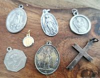 Photo showing seven religious pendants variously shaped including oval, round, hexagonal and cross pendant with metal finish, displayed on wooden surface.
